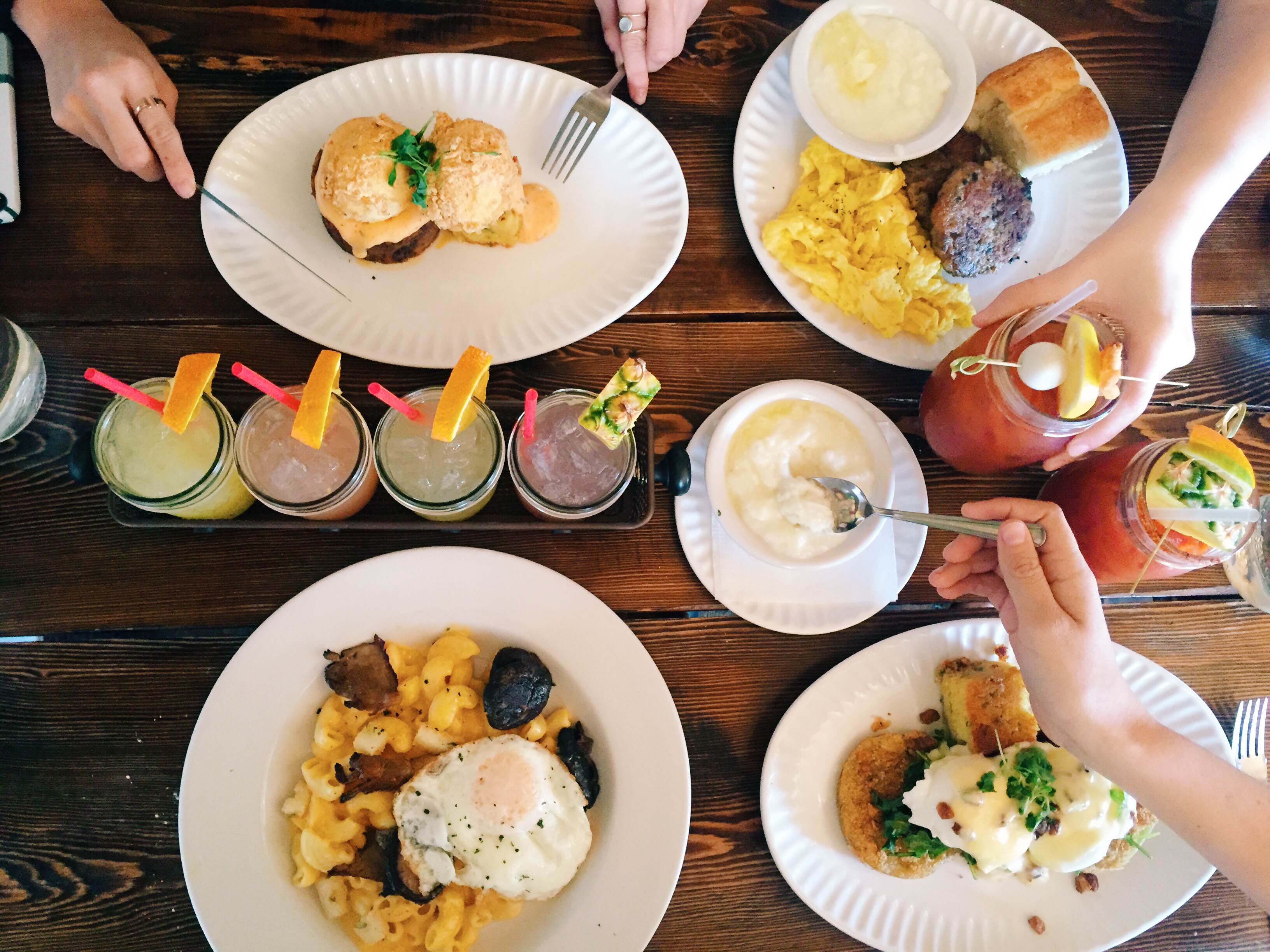 Overhead view of a communal brunch spread at Sassafras American Eatery with golden comfort food plates, colorful milkshakes, and loaded Bloody Marys